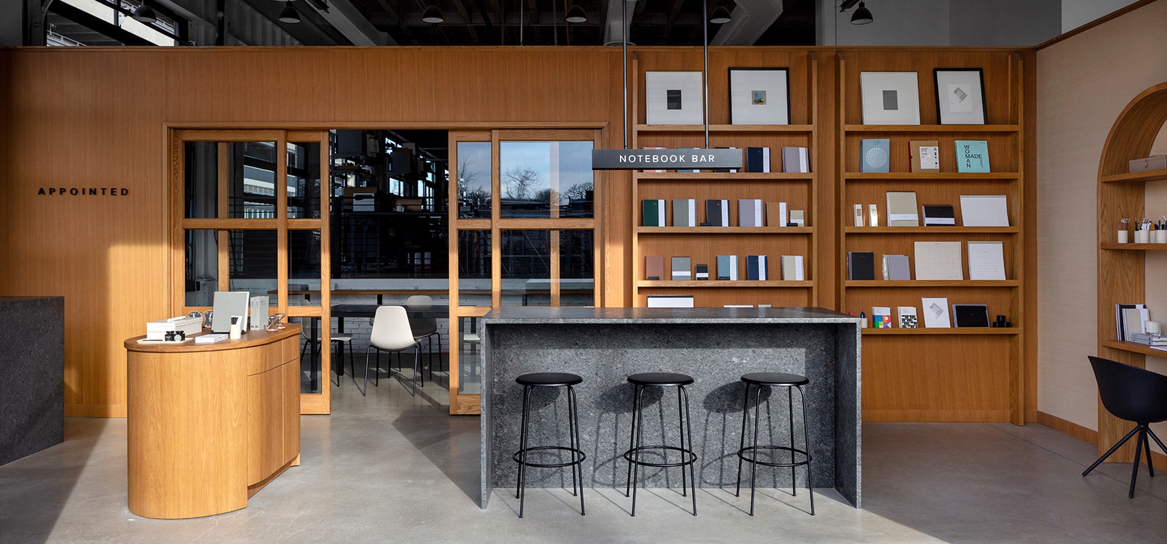 The Appointed District Shop is half drenched in sunlight. In site, you can see our Notebook bar, wall of signature products, and various stationery accessories on custom wood shelving.