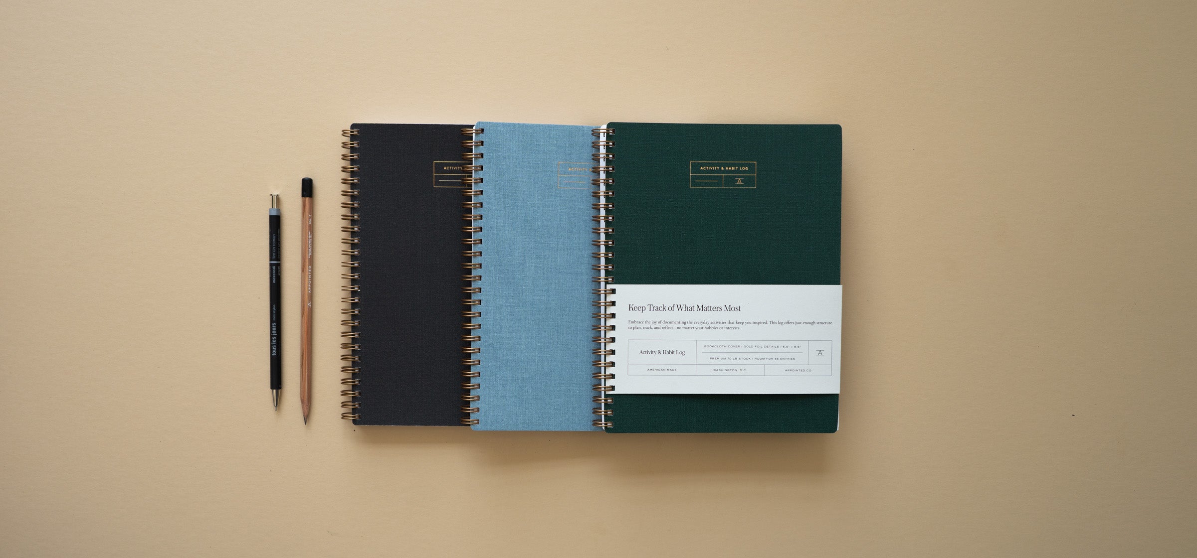 The Appointed Activity & Habit Log sits stacked against a beige background in alternating colors left to right. Two writing tools sit aside to the left.