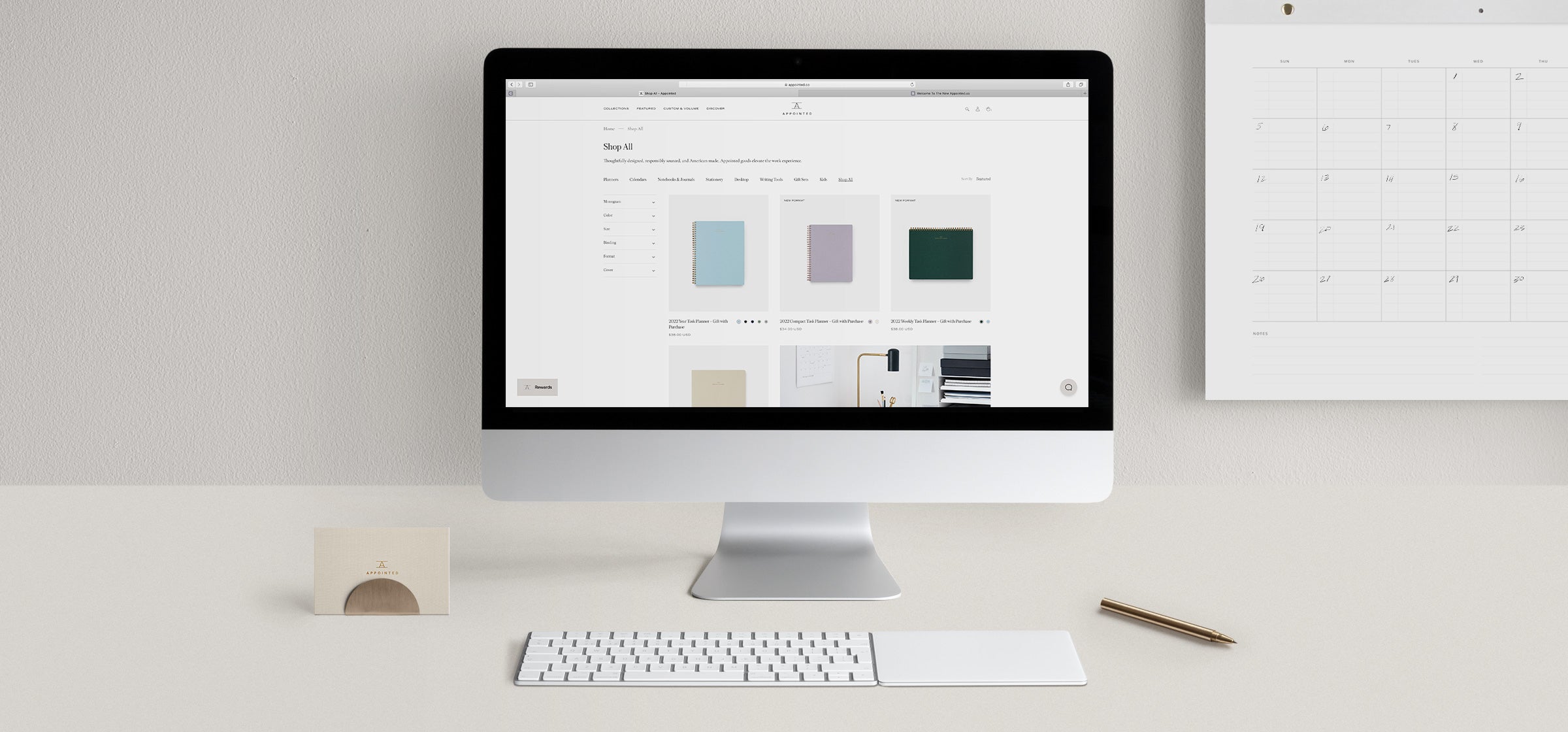 A desktop computer open to the appointed.co website sits on a cool gray desk with desk accessories & a wall calendar