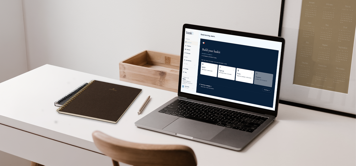 A laptop sits on a desk with a notebook and pencil set aside. On the laptop, the digital tool, Baskit, is open.